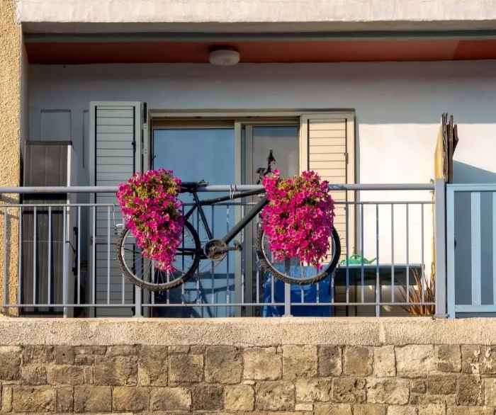 Oryginalny wystrój balkonu mieszkania. Szeroki balkon z kwiatami i miejscem na rower. 