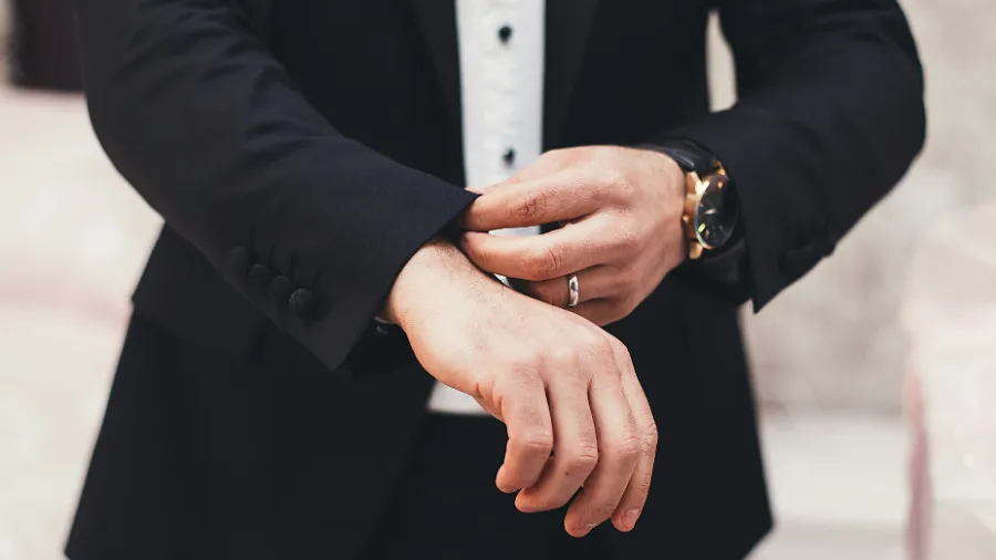 Mężczyzna w czarnym garniturze zegarkiem na ręce poprawia mankiet koszuli.