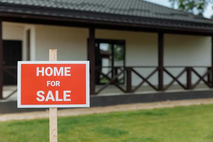 Nowoczesny, parterowy dom na sprzedaż z tablicą 'HOME FOR SALE' na przednim trawniku