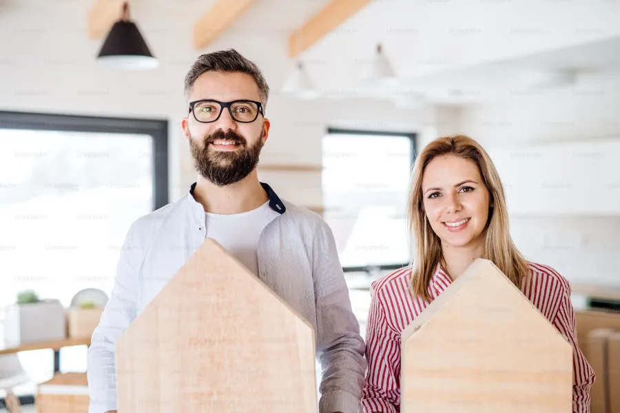 Dwoje uśmiechniętych ludzi trzymających drewniane modele domów w jasnym, nowoczesnym biurze