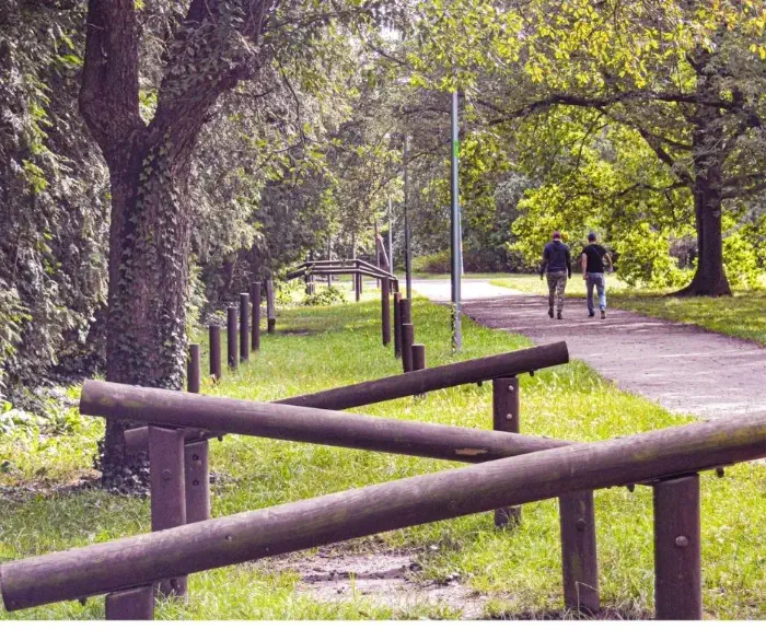 Widok pełnego zieleni Parku Grabiszyńskiego we Wrocławiu. W tle spaceruje dwóch mieszkańców. 