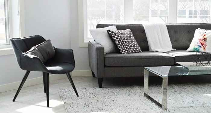 nowoczesny czarny fotel stoi obok szarej kanapy i metalowo-szklanego stolika. 