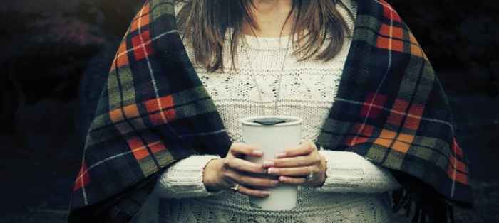 Kobieta w ciepłym, jesiennym szalu. Trzyma w rękach gorącą herbatę.
