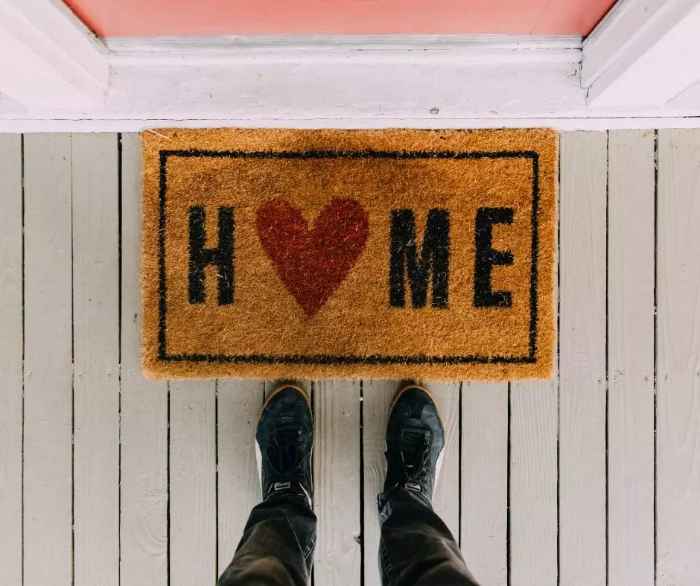 Wycieraczka z czerwonym sercem i napisem "home" na drewnianej posadzce przed drzwiami wejściowymi