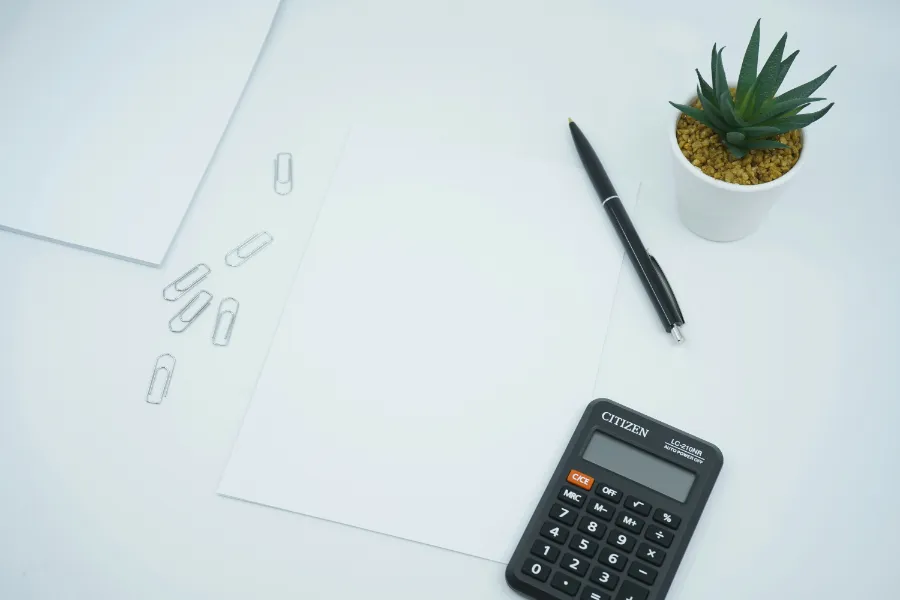 Biurko z czystymi arkuszami papieru, czarnym długopisem, kalkulatorem i doniczką z rośliną