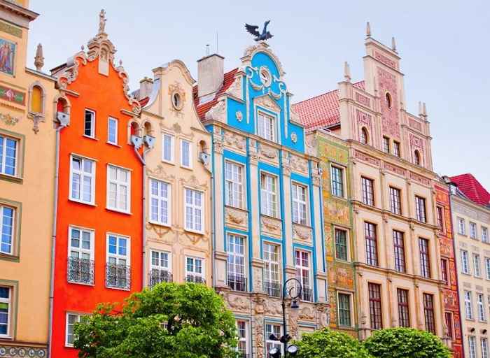 Kolorowe budynki z ozdobnymi wykończeniami na rynku w Gdańsku. Pod budynkami czarna latarnia i zielone drzewa