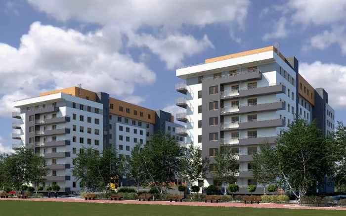 Nowe osiedle mieszkaniowe z nowoczesnymi blokami mieszkalnymi i terenami zielonymi. Nad budynkami jasne niebo z białymi chmurami.