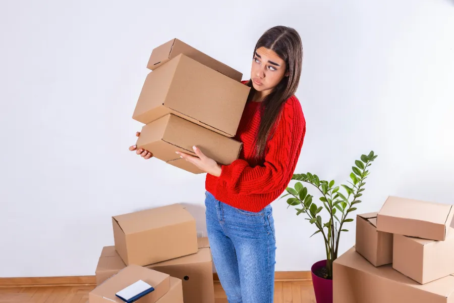  Młoda kobieta trzyma stos kartonowych pudeł w przeprowadzce, wydaje się zmartwiona lub zaskoczona