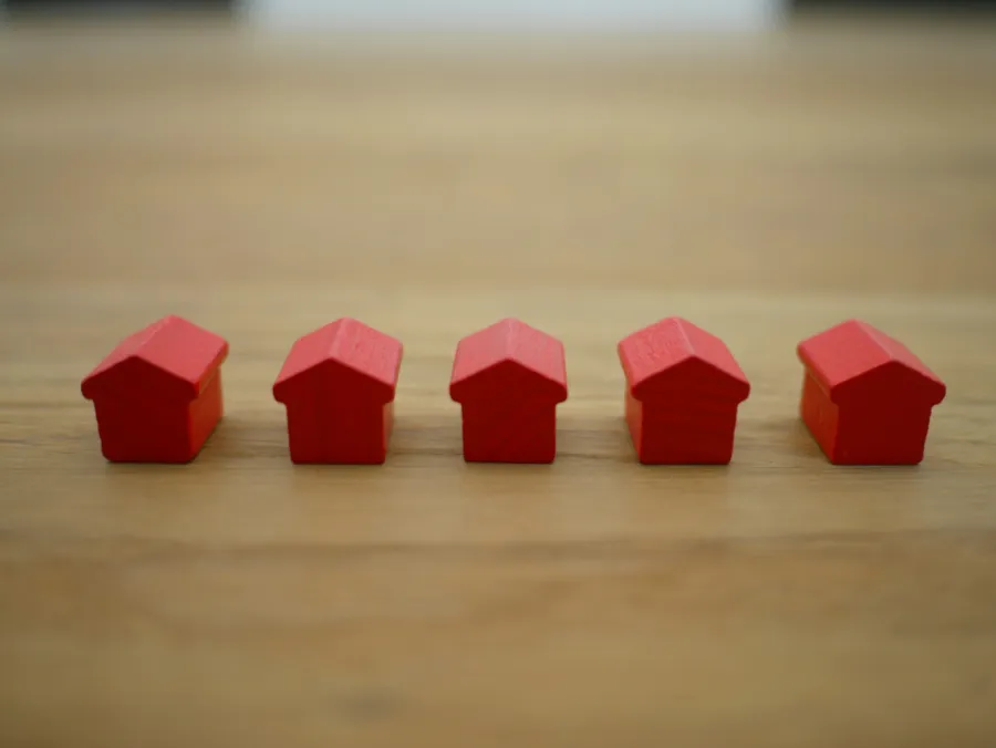 Małe, czerwone modele domów ustawione na drewnianym stole, reprezentujące inwestycje w nieruchomości