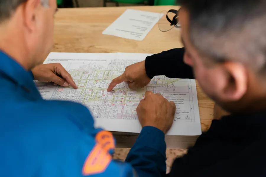 Dwóch mężczyzn analizujących plan architektoniczny lub mapę działek na drewnianym stole