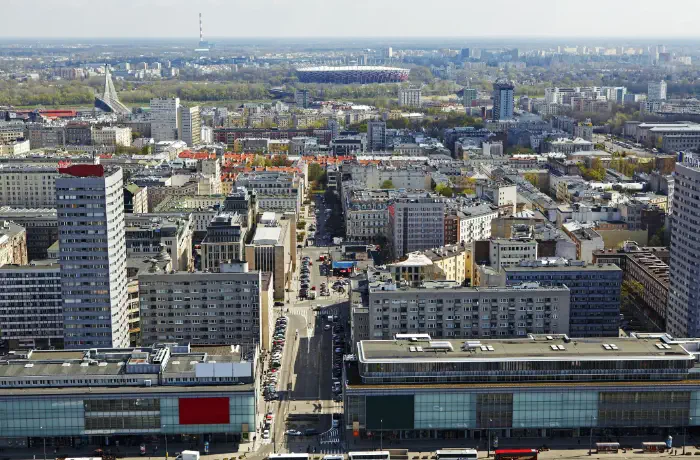 Widok z lotu ptaka na architekturę stolicy Polski za dnia. W tle PGE Narodowy, elektrownia i budynki aż po rozmyty horyzont