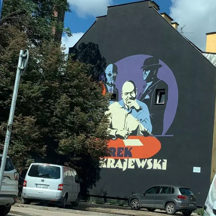 Widok Muralu Marka Krajewskiego we Wrocławiu. Zdjęcie Muralu robione na ulicy, w otoczeniu drzew. 