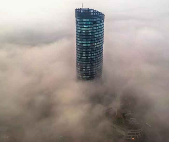 Zdjęcie wieżowca Sky Tower z lotu ptaka. W powietrzu unosi się mgła, która zasłania widok całego osiedla.